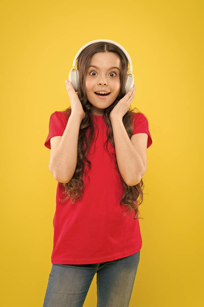 Face the sound. Adorable little girl listening to sound track on yellow background. Cute small child wearing headphones playing electronic sound. Relaxing with melodious sound - 写真・画像