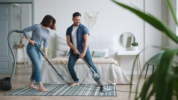 Man and woman having fun at home vacuuming carpet in bedroom dancing singing - Filmati, video