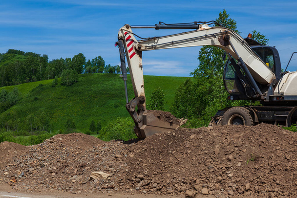 A white excavator stands on a heap of rubble and stones in the i - 写真・画像
