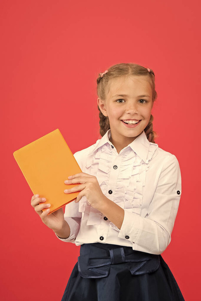 All of her knowledge is from book. Adorable small girl holding book on red background. Cute little child with book knowledge in hands. Knowledge skills. Knowledge day or September 1, copy space - Foto, imagen