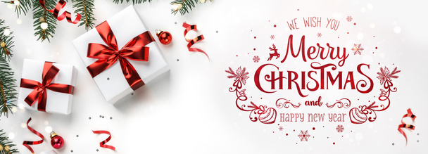 Vrolijke kersttekst op witte achtergrond met geschenkdozen, sparren takken, rode decoratie. Kerstmis en Nieuwjaar wenskaart, bokeh, licht. Flat lay, bovenaanzicht, wintervakantie, brede compositie - Foto, afbeelding