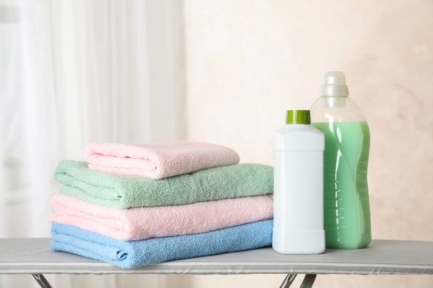 Pilha de toalhas limpas e líquido de lavandaria na tábua de engomar, cópia
  - Foto, Imagem
