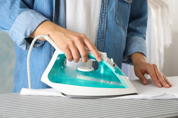 Young woman ironing shirt on ironing board, close up - Foto, afbeelding