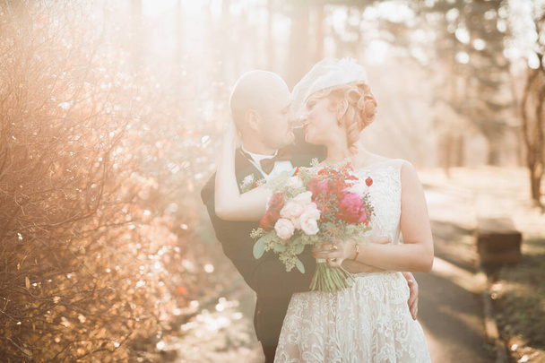 Romantisches, märchenhaftes, glückliches Brautpaar, das sich im Park umarmt und küsst, Bäume im Hintergrund - Foto, Bild