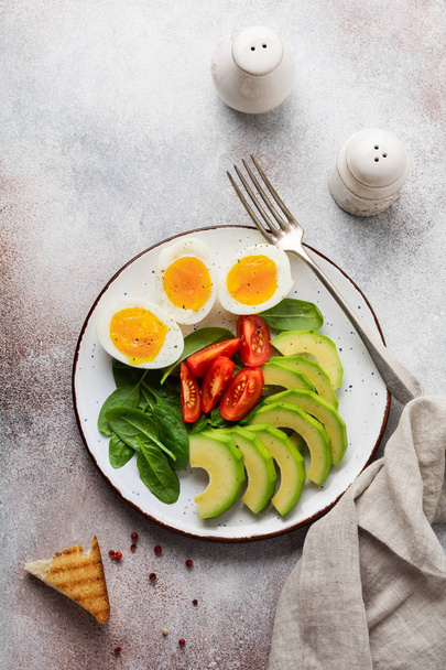 Healthy vegetarian salad breakfast. Spinach leaves, tomato, avocado and boiled egg on gray plate and gray concrete old background. Buddha bowl. Top view.  - Fotoğraf, Görsel