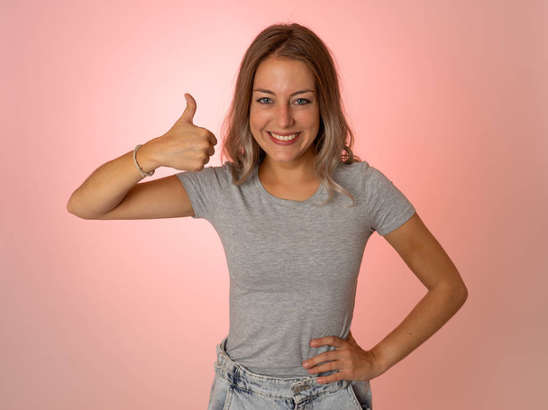 Portrait of beautiful young woman showing thumbs up sign feeling cheerful, happy and satisfied. Young happy student woman making thumb up in joyful approval gesture isolated on pink background. - Photo, Image