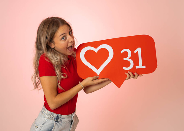 Attractive woman holding heart symbol of like and love social media notification icon happy with followers and fans on the internet. Girl loving having likes In social media obsession and networking. - Photo, Image