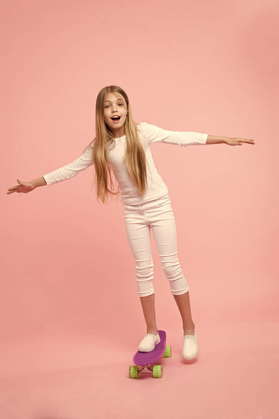Regenerating her energy skateboarding. Adorable little child performing skateboarding tricks on pink background. Cute small girl skateboarding on violet penny board. Go skateboarding day - Фото, изображение