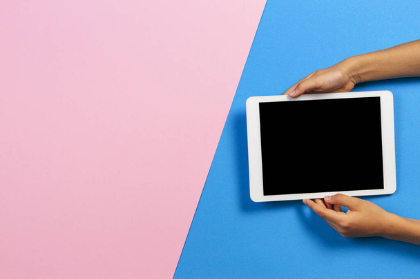 Mains d'enfant avec ordinateur tablette sur fond rose pastel et bleu clair
 - Photo, image