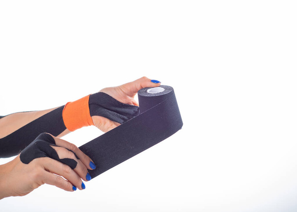 Physiotherapy for a diseased wrist. Alternative medicine. Adhesive tape for athletes with injuries. Support for an injured finger. Female hands on a white background hold a roll of kinesiotape. - Photo, image
