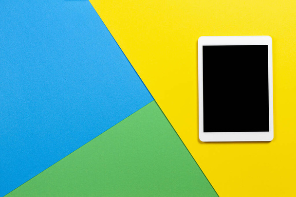 Digital tablet computer on light blue, green and yellow background. Top view - Photo, Image