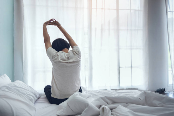 Homem asiático sentado na cama e esticando os braços durante o conde
 - Foto, Imagem