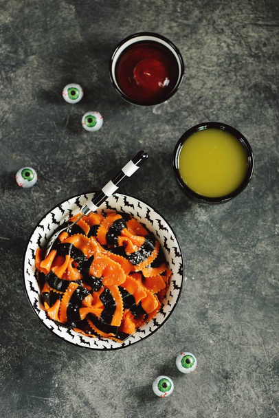 Pasta farfalle in een bord met vleermuizen patroon met olijfolie, parmezaanse kaas, tomatensaus en sinaasappelsap voor Halloween feest. Halloween achtergrond. Bovenaanzicht.  - Foto, afbeelding