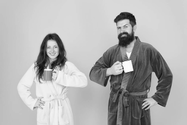 Every morning begins with coffee. Couple in bathrobes with mugs. Man with beard and sleepy woman enjoy morning coffee or tea. Guy in bath clothes hold tea coffee. Start new day. Breakfast concept - Fotografie, Obrázek