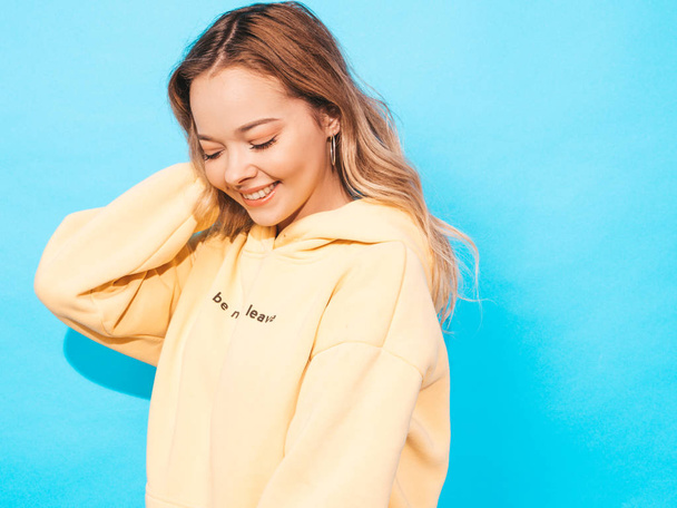 Portrait of young beautiful smiling girl in trendy summer hipster yellow hoodie.Sexy carefree woman posing near blue wall. Positive model having fun - Fotografie, Obrázek