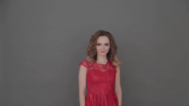 Beautiful young girl in a red dress posing on a gray background. - Video