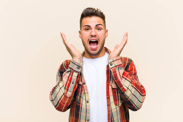 young hispanic man feeling shocked and excited, laughing, amazed and happy because of an unexpected surprise against isolated background - Photo, Image