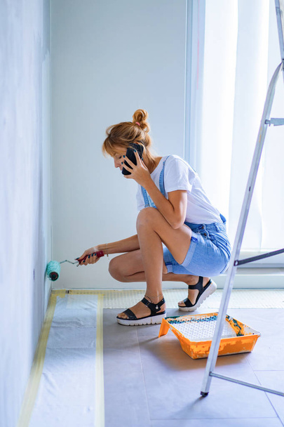 joven hermosa mujer hace reparaciones en el apartamento, pinta las paredes con un rodillo. Trabajos molares
. - Foto, Imagen