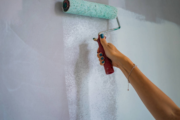 young beautiful woman makes repairs in the apartment, paints the walls with a roller. Molar work. - 写真・画像