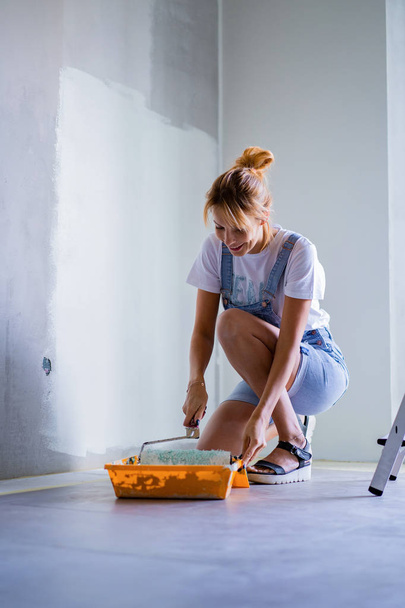 young beautiful woman makes repairs in the apartment, paints the walls with a roller. Molar work. - Foto, immagini