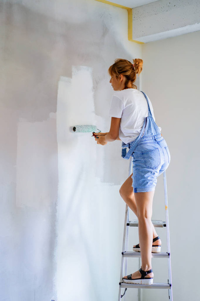 young beautiful woman makes repairs in the apartment, paints the walls with a roller. Molar work. - Foto, afbeelding
