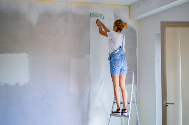 young beautiful woman makes repairs in the apartment, paints the walls with a roller. Molar work. - Foto, Imagen