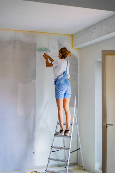 young beautiful woman makes repairs in the apartment, paints the walls with a roller. Molar work. - Foto, Imagem