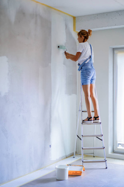 young beautiful woman makes repairs in the apartment, paints the walls with a roller. Molar work. - Valokuva, kuva