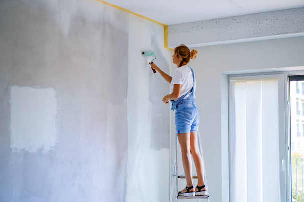 young beautiful woman makes repairs in the apartment, paints the walls with a roller. Molar work. - Foto, Bild