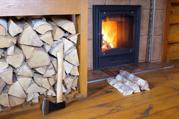 Eisenbeil und Birkenbrennholz am Kamin in einem Landhaus.  - Foto, Bild
