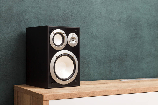 Single modern black audio speaker in interior on wooden desk near the wall - Foto, imagen