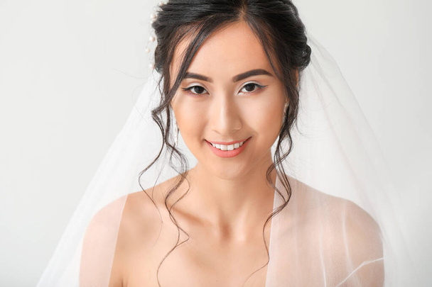 Beautiful young Asian bride on light background - Фото, зображення