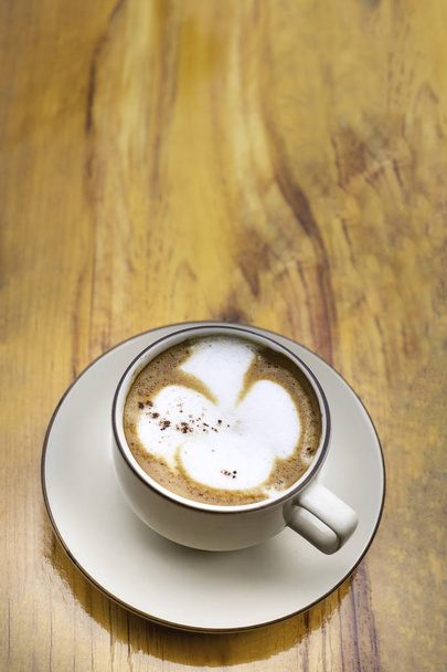 Detailní záběr Latte art nebo cappuccino bílý šálek kávy s talířem na dřevěném stole s kopírovacím prostorem. pohled shora - Fotografie, Obrázek