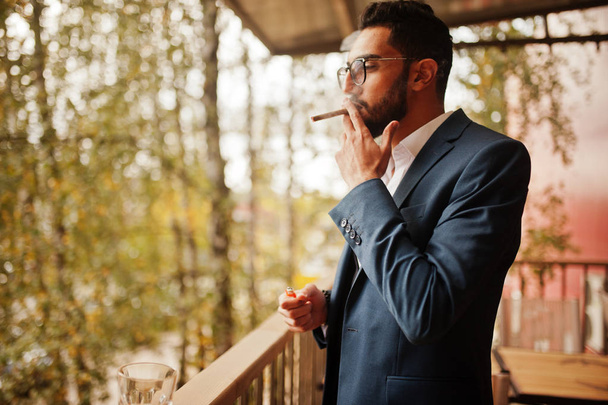 Knappe goed geklede Arabische man rookt sigaar op balkon van pub. - Foto, afbeelding
