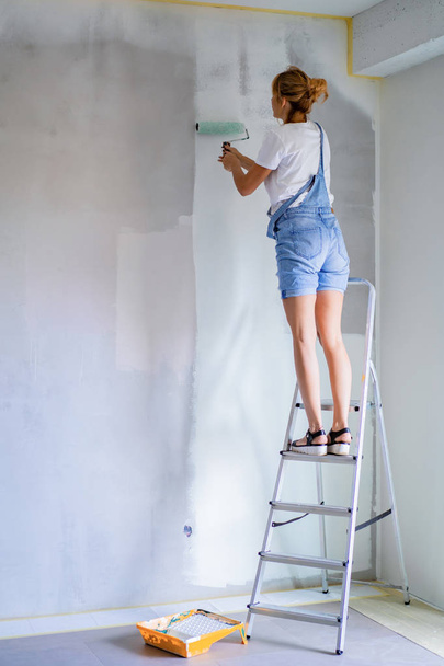 young beautiful woman makes repairs in the apartment, paints the walls with a roller. Molar work. - Fotó, kép