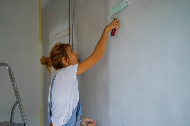 young beautiful woman makes repairs in the apartment, paints the walls with a roller. Molar work. - Photo, image