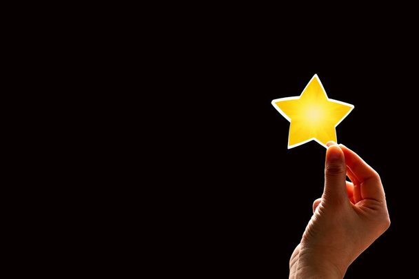 eine Frau schenkt einen Stern. das Konzept einer positiven Bewertung, Bewertungen und Feedback auf schwarzem Hintergrund. - Foto, Bild