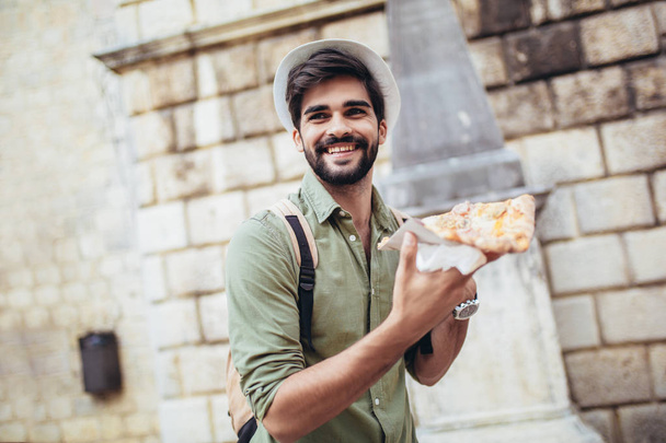 Nuori komea rento mies syö pizzaa ulkona
 - Valokuva, kuva