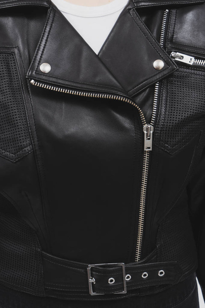 Black leather jacket with perforated elements. Metal zippers, clasps and buttons. Classic clothes for biker. Detailed closeup view. White t-shirt. Vertical photo. - Photo, Image
