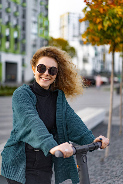 Young beautiful woman riding an electric scooter to work, modern girl, new generation, electric transport, ecology, ecological transport, sunset - Photo, Image