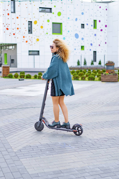 Joven hermosa mujer montando un scooter eléctrico para trabajar, chica moderna, nueva generación, transporte eléctrico, ecología, transporte ecológico, puesta de sol - Foto, imagen