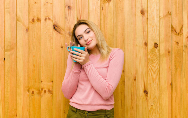 young pretty blonde woman with a coffee cup against wood wall - Fotoğraf, Görsel