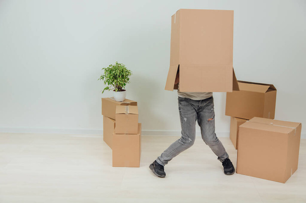 Funny man is standing with cardboard box on his head, hesitating, not seeing where to go. Handsome young man moving into new house. - Фото, зображення