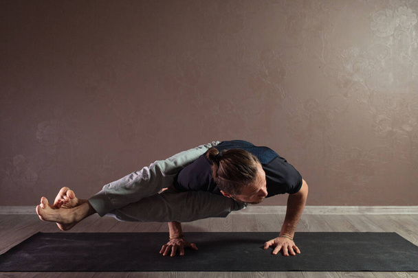 Mladý sportovní muž cvičí jógu, medituje v póze Half Lotus, cvičí, nosí sportovní oblečení, v interiéru po celou dobu, hnědé jóga studio - Fotografie, Obrázek