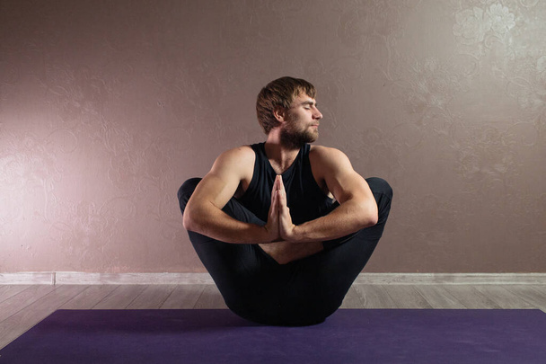 Jovem homem esportivo praticando ioga, meditando em Half Lotus pose, exercitando-se, vestindo sportswear, comprimento total interior, estúdio de ioga marrom
 - Foto, Imagem