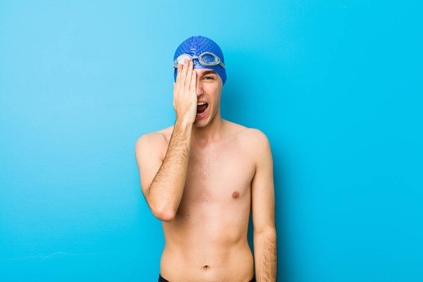 Jonge zwemmer die plezier heeft met het bedekken van de helft van het gezicht met palm. - Foto, afbeelding