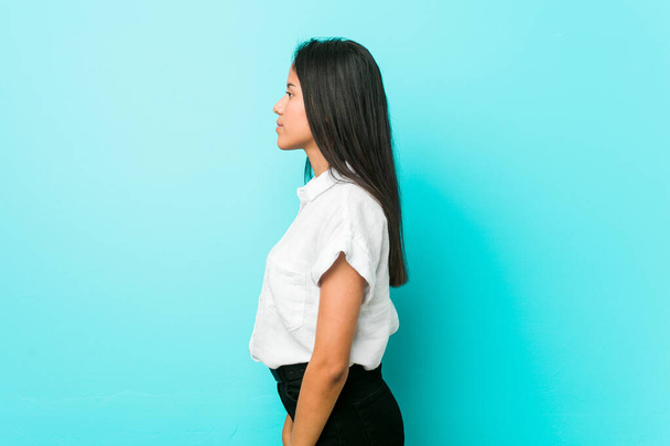 jonge hispanic koele vrouw tegen een blauwe muur staren links, zijwaarts poseren. - Foto, afbeelding