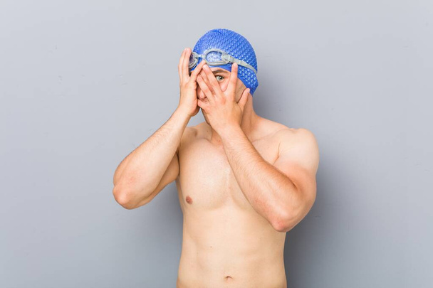 Jeune nageur professionnel cligner des yeux à travers les doigts effrayé et nerveux
. - Photo, image