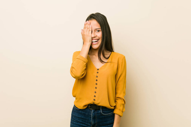Young hispanic woman against a beige background having fun covering half of face with palm. - Photo, image