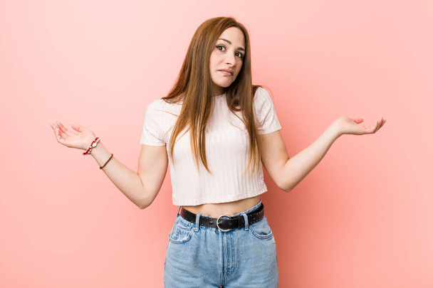 Young redhead ginger woman against a pink wall doubting and shrugging shoulders in questioning gesture. - Foto, imagen